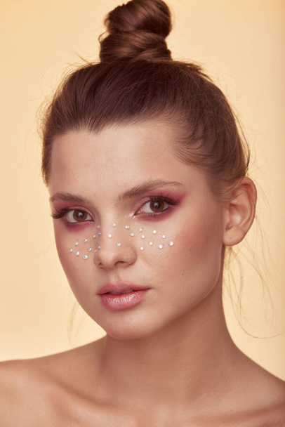 Fashion creative make up. Beautiful portrait of young woman with clean fresh skin and bright make up with rhinestones freckles on her face posing on a yellow background - Fotó, kép