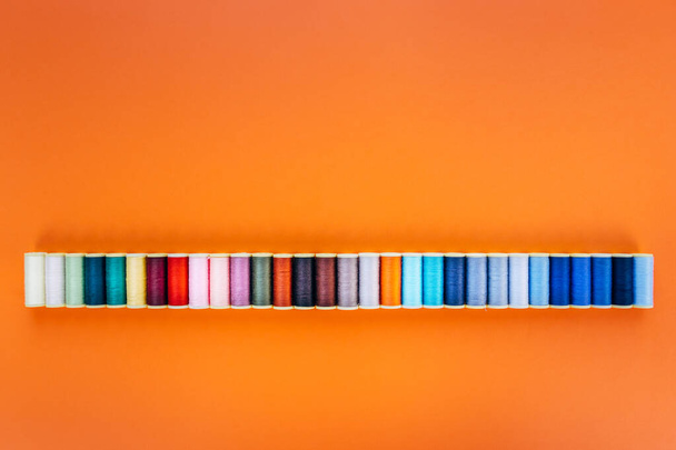 wide panorama background with colorful sewing cottons spools isolated on orange background - 写真・画像