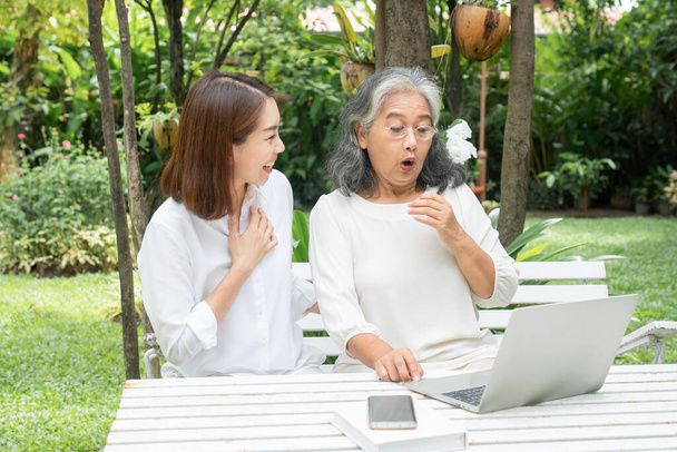 Hija asiática enseñando anciana anciana uso de medios sociales en línea en computadora portátil después de la jubilación. Concepto de tecnología de aprendizaje y adaptación de las personas mayores - Foto, Imagen