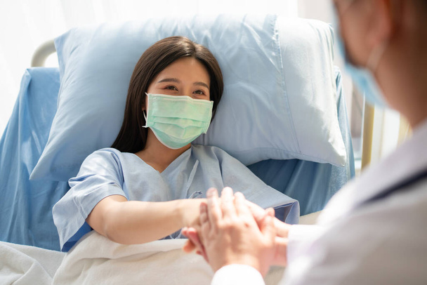 Vrouwen Aziatische artsen houden de patiëntenhand vast en moedigen medisch advies aan terwijl ze de gezondheid van de patiënt in bed controleren. Concept van zorg en mededogen - Foto, afbeelding