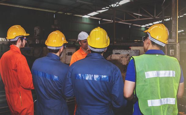 Der Ingenieur trägt einen Helm, ruft zu einem Treffen des Ingenieurteams auf, alle Arbeiter kommen, um über die Arbeitsergebnisse zu berichten, um die Richtlinien des Unternehmens zur Sicherheit am Arbeitsplatz einzuhalten. - Foto, Bild