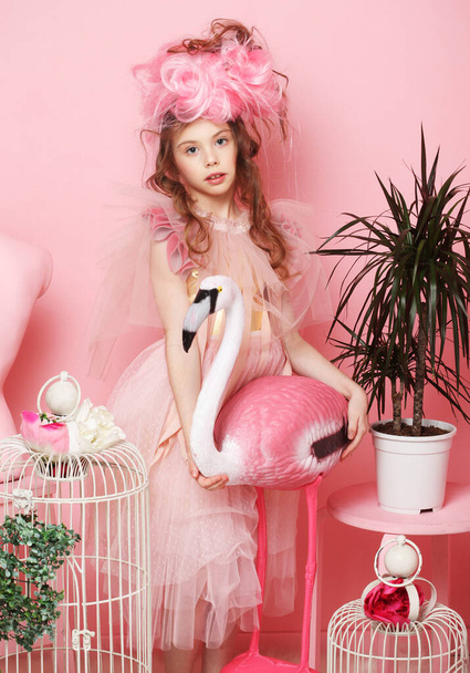 Adorable little girl in a fairy costume and make-up holding a flamingo, pink tones, fairy tale, dream. - Foto, afbeelding