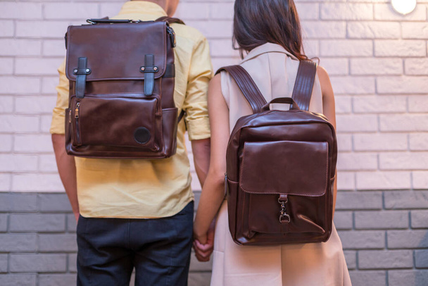 На спине мужчины и женщины с коричневым кожаным рюкзаком. Мужчина и женщина держатся за руки и представляют кожаные сумки. Односексовая сумка на продажу. - Фото, изображение