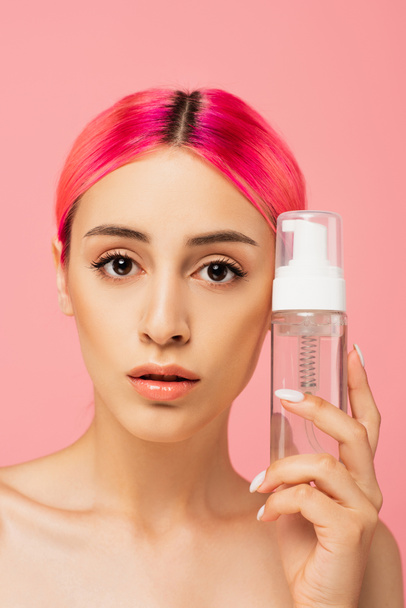 young woman with colorful hair holding bottle with toner isolated on pink  - Valokuva, kuva