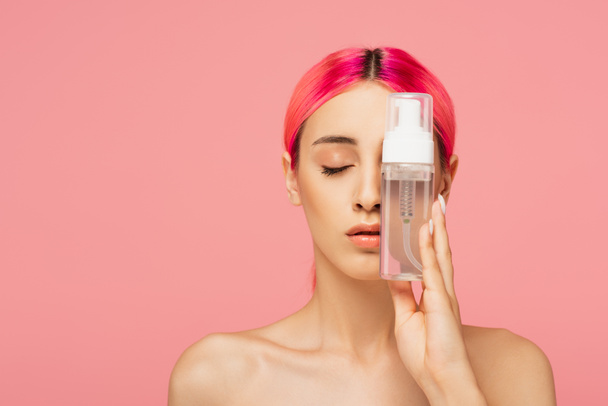mujer joven con el pelo teñido y los ojos cerrados sosteniendo botella con producto de limpieza aislado en rosa  - Foto, imagen