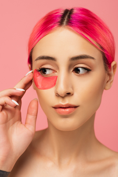 jeune femme aux cheveux colorés appliquant patch hydratant pour les yeux isolé sur rose  - Photo, image
