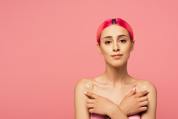 young woman with colorful hair applying lotion on bare shoulders isolated on pink  - Foto, Imagem
