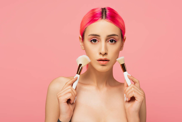 mladá žena s barevnými vlasy drží kosmetické štětce izolované na růžové  - Fotografie, Obrázek