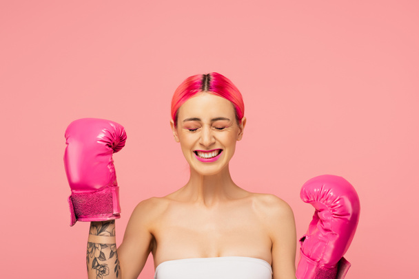 šťastná mladá žena s barvenými vlasy a světlé make-up v boxerských rukavicích izolovaných na růžové  - Fotografie, Obrázek