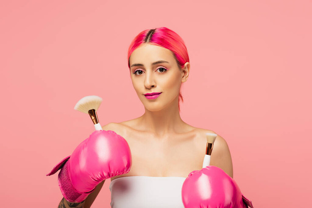 young woman with dyed hair and boxing gloves holding cosmetic brushes isolated on pink  - Fotoğraf, Görsel