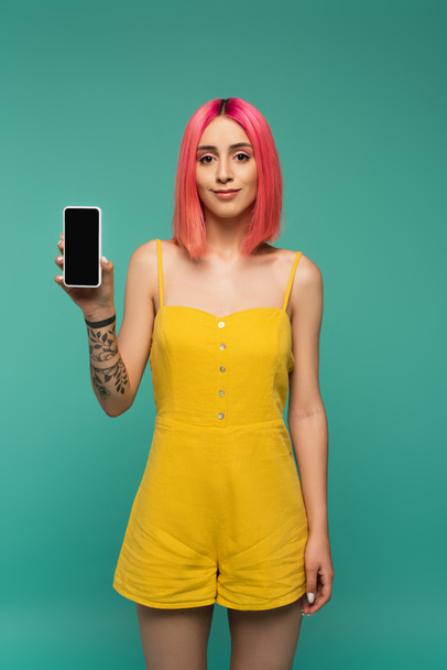 pleased young woman with pink dyed hair holding smartphone with blank screen isolated on turquoise - Fotoğraf, Görsel