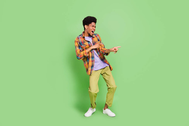 Photo of sweet cute dark skin man wear plaid shirt smiling dancing pointing fingers empty space isolated green color background - Fotó, kép