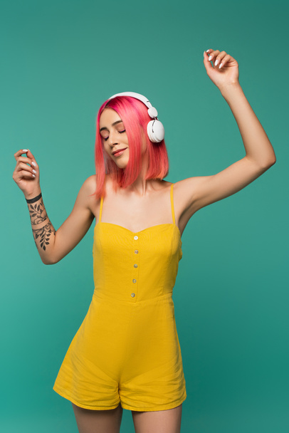 fiatal nő rózsaszín festett haj hallgat zenét fejhallgató és tánc elszigetelt kék - Fotó, kép