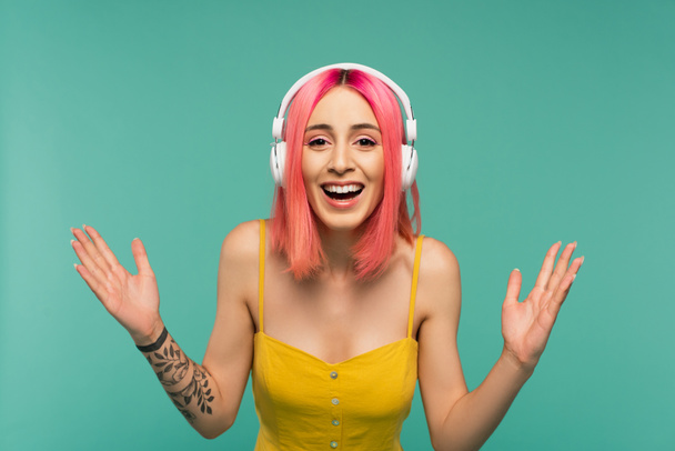 excited young woman with pink dyed hair listening music in headphones isolated on blue - Fotó, kép