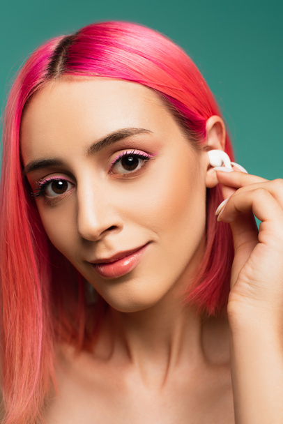young woman with pink dyed hair adjusting wireless earphone isolated on blue - Photo, image