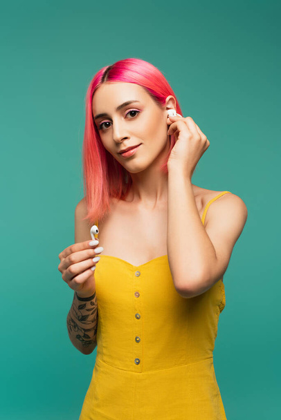 pretty young woman with pink dyed hair holding wireless earphones isolated on blue - Φωτογραφία, εικόνα