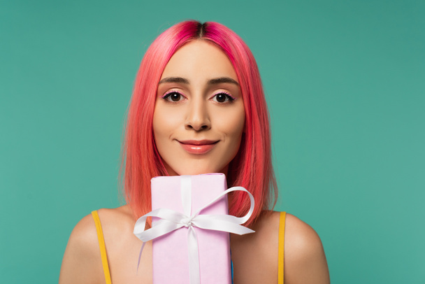 smiling young woman with pink dyed hair holding wrapped present isolated on blue  - Фото, изображение