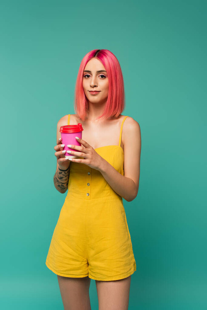 young woman with pink dyed hair holding paper cup with coffee to go isolated on blue  - Foto, afbeelding