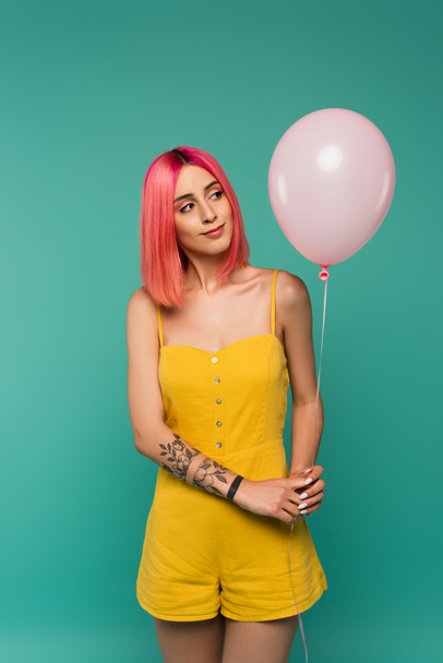 curious young woman with pink dyed hair looking at balloon isolated on blue  - Foto, Bild