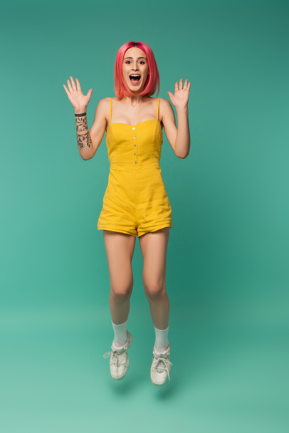 full length of excited young woman with pink dyed hair jumping on blue  - Foto, Imagem