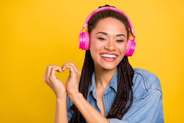 Photo of young afro girl happy positive smile show heart figure listen earphones isolated over yellow color background - Fotografie, Obrázek
