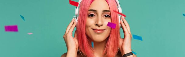 щаслива молода жінка з рожевим фарбованим волоссям в бездротових навушниках поблизу барвистих конфетті на синьому, банер
 - Фото, зображення