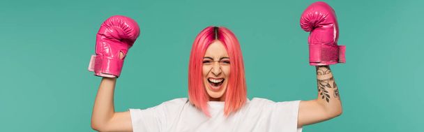 izgatott fiatal nő rózsaszín festett haj boksz kesztyű elszigetelt kék, banner - Fotó, kép