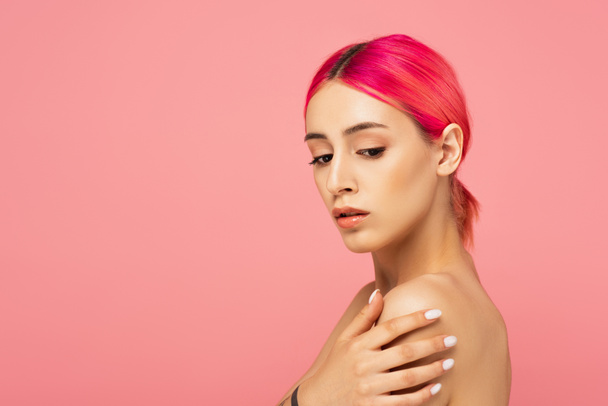 hübsche junge Frau mit bunten Haaren, die die nackte Schulter berührt, isoliert auf rosa - Foto, Bild