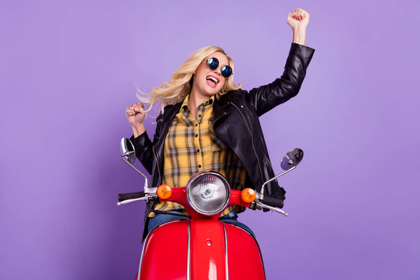 Portrait of lovely cheerful wavy-haired girl riding moped having fun rejoicing isolated over bright violet purple color background - Foto, Imagem