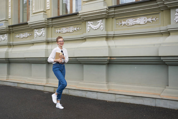 φοιτητής με γυαλιά περπατώντας γύρω από την πόλη με μια επικοινωνία βιβλίο - Φωτογραφία, εικόνα