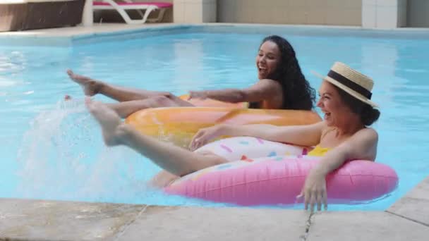 Erholung und Unterhaltung auf dem Wasser, erfolgreicher Urlaub, Hotelbuchung. Zwei fröhliche, vielfältige junge Freundinnen, Millennialmädchen, die wunderbare Sommerferien genießen, Schwimmbadwerbung - Filmmaterial, Video