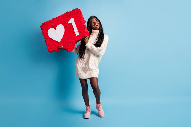 Photo of shiny cute dark skin woman dressed winter clothes holding big like poster looking empty space isolated blue color background - Photo, image
