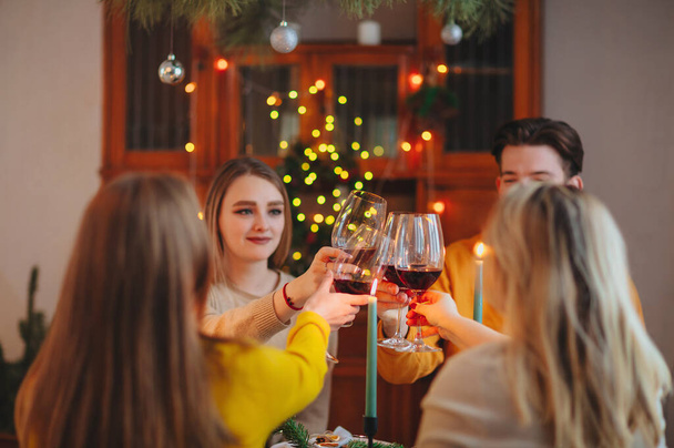 Szczęśliwi młodzi przyjaciele brzęczenie kieliszki wina nad stołem urządzone na Boże Narodzenie w domu - Zdjęcie, obraz