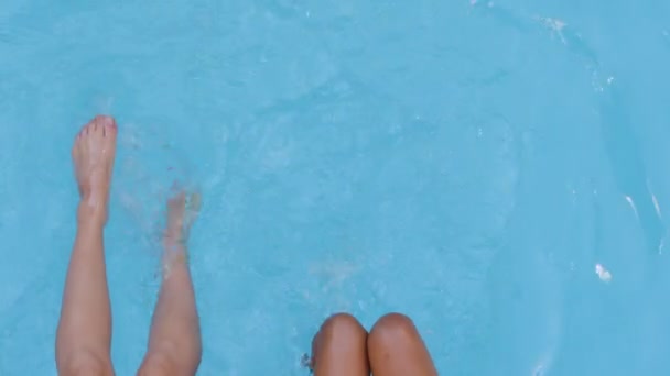 Vista superior close-up dois pares bronzeado magro esbelto belas pernas femininas balançando agitando fazendo onda na piscina azul de verão. Senhora pé turístico subaquático no spa, lazer fim de semana resort junto à piscina - Filmagem, Vídeo