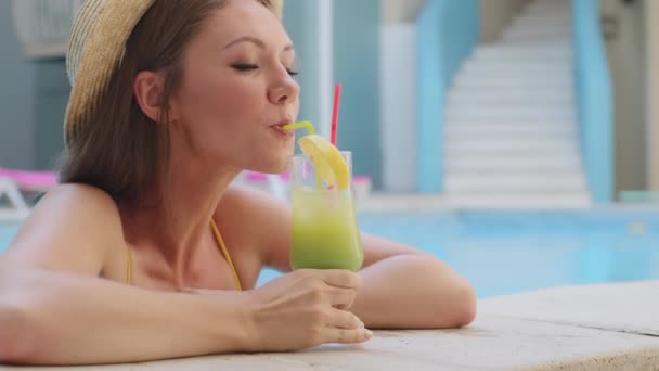 Carino giovane ragazza europea in costume da bagno e cappello rilassante nella piscina estiva spa hotel bere cocktail di ghiaccio attraverso la paglia. Attraente turista donna millenaria godendo piacevole vacanza con bicchiere di bevanda - Filmati, video