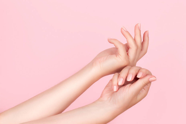 Kobiece ręce z pięknym manicure - różowe nagie paznokcie na różowym tle. Koncepcja pielęgnacji paznokci - Zdjęcie, obraz