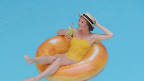 Feliz despreocupado Hermosa milenaria chica de piel clara europea en traje de baño flotando en boya de vida de natación inflable naranja con vaso de bebida refrescante. Atractiva joven bebiendo cóctel - Metraje, vídeo