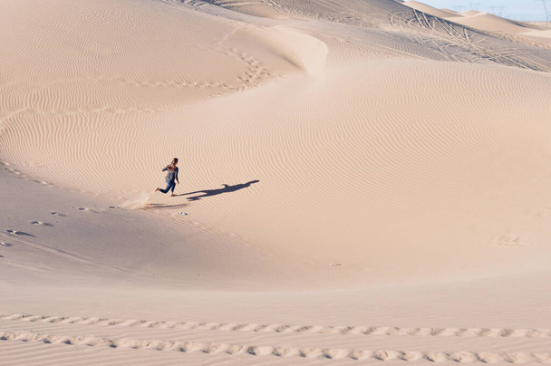 A high angle shot of a female running on sand dunes in a desert - Photo, image
