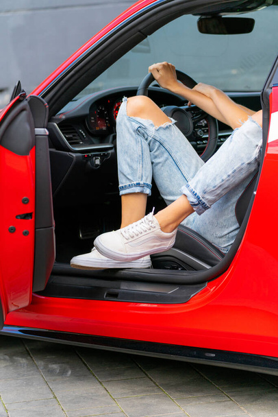 A young trendy fashionable woman in blue ripped jeans sitting in a beautiful red car - Foto, Bild