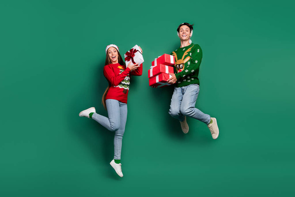 Photo of crazy carefree couple hold present boxes jump wear ugly sweater isolated green color background - Φωτογραφία, εικόνα