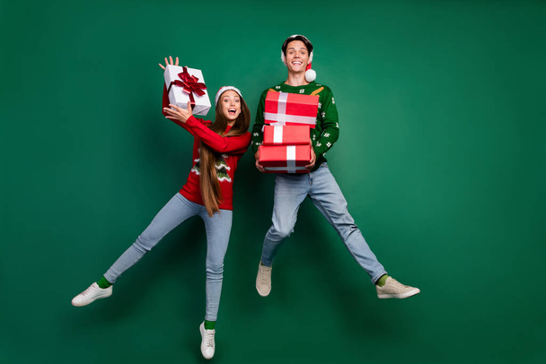 Photo of funny crazy couple hold pile giftbox enjoy jump flight wear hat ugly pullover isolated green color background - Foto, Imagem