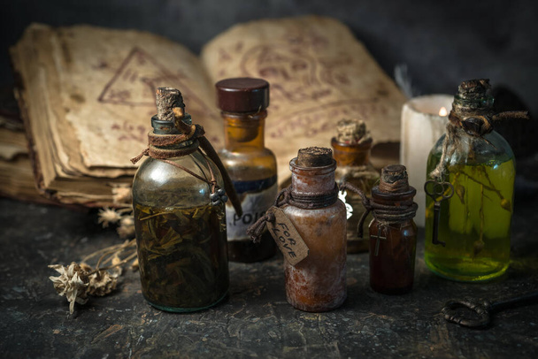 ボトルの魔法のポーション、木製の背景の古代の本や魔女のハーブ、ハロウィーンのテーマ - 写真・画像