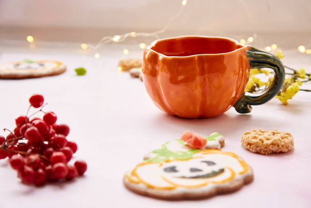 Halloween kreatív koncepció: sütőtök csésze és édes cookie-k formájában ünnepi sütőtök. Atmoszférikus esztétikai őszi hangulat vagy trükk vagy csemege koncepció. Viburnum és kandírozott gyümölcs dekoráció. - Fotó, kép