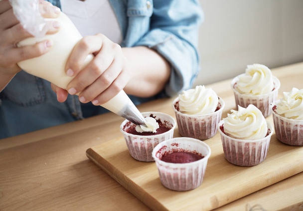 Lifestyle, food, people and small business concept: A young woman decorates muffins with white cream and berries. - Foto, imagen