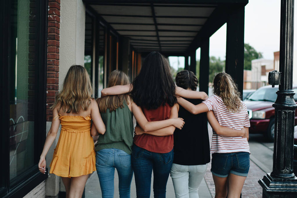 Вид ззаду на групу жіночих друзів, які обіймаються і ходять на відкритому повітрі
 - Фото, зображення