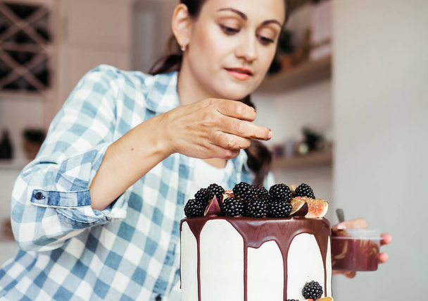 Lifestyle, food, people concept: Pastry chef in the kitchen decorating a cake of chocolate and berries - Foto, Imagen