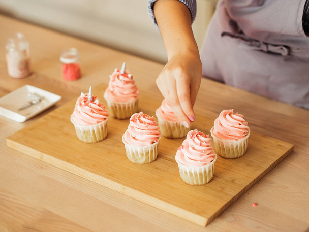 A young woman decorates muffins with white cream in her kitchen. - Foto, Bild