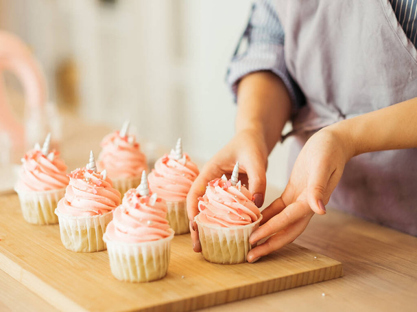 A young woman decorates muffins with white cream in her kitchen. - Foto, Imagem