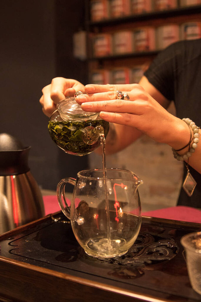 Зеленый чай, стеклянный чайник с чайными листьями, чай наливают в чашку на чайной церемонии - Фото, изображение