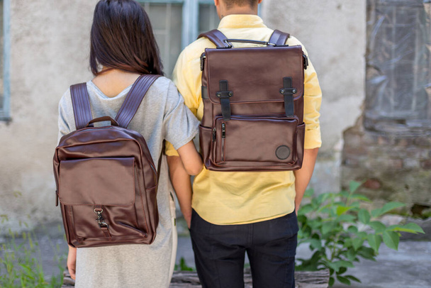 Back of woman and man with brown leather backpack. Man and woman holding hands and presenting leather bags. Unisex bag for sale. - Photo, Image